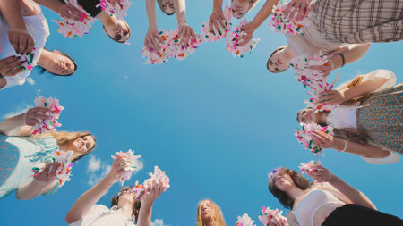 High school students in a circle, holding bright confetti against a vivid summer skyの写真素材