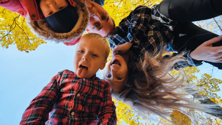 Cheerful family laughing, playing amid vibrant autumn foliage, creating joyful memories in sunlit park settingの写真素材