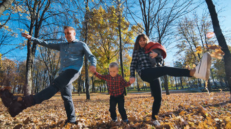 Family spending autumn afternoon walking through fallen leaves, laughing and playing together in golden hued park landscapeの写真素材