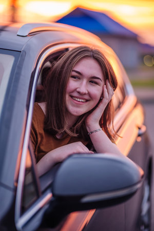 Smiling female driver relaxing inside vehicle, golden sunlight illuminating interior during scenic...