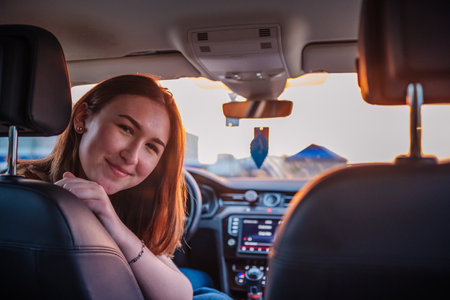 Redheaded teenage passenger smiling contentedly, basking in golden sunset light while relaxing during leisurely road trip journeyの写真素材