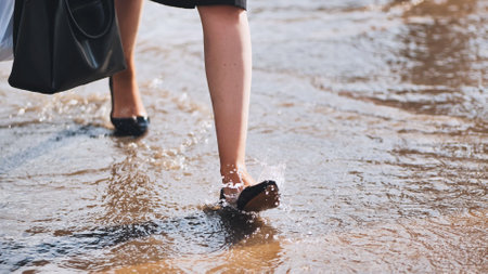 Businesswoman carefully wading through dirty flood water on urban street after heavy rain, facing challenge and riskの写真素材