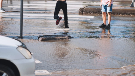 Teenage friends jumping over flooded crosswalk after heavy urban rainstorm, splashing water...