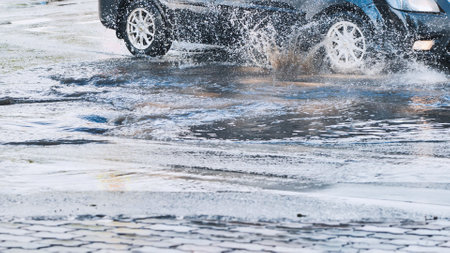 High speed vehicle splashing water while driving through roadside puddle, generating dramatic spray patternの写真素材