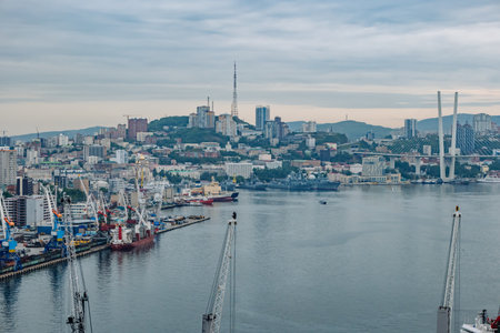 Cranes, cargo ships, and russian navy warships fill the foreground of golden horn bay, with vladivostoks skyline rising behindの写真素材