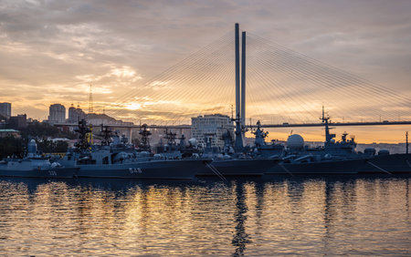 Russian navy warships are anchored in vladivostok harbor at sunset under the zolotoy rog bridge,...