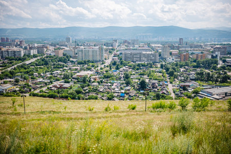 Scenic view of krasnoyarsk, russia, showcasing residential houses, apartment buildings, and mountains under a cloudy skyの写真素材