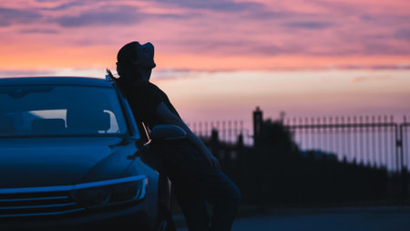 Relaxed woman silhouetted against car, resting during sunset after driving long highway stretchの写真素材
