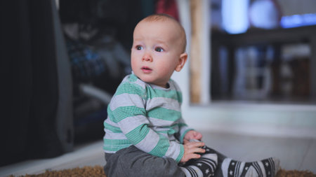 Infant sitting barefoot, exploring tiny toes while gazing sideways, capturing pure childhood wonder in soft, warm indoor environmentの写真素材