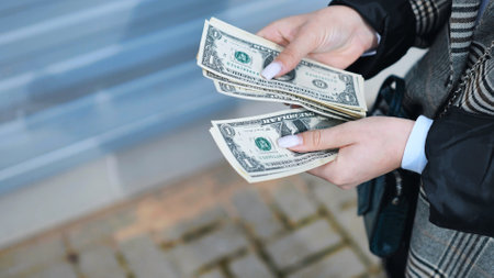 Businesswoman counting cash in open air setting, tracking expenses and managing personal budget with careful financial strategyの写真素材