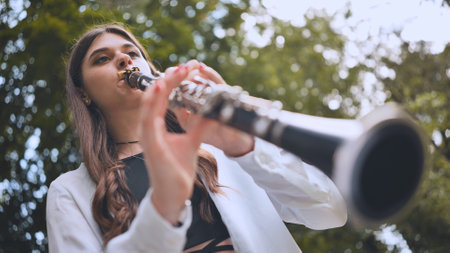Young musician performing clarinet amid lush green park, expressing melodic passion surrounded by tranquil natural landscapeの写真素材