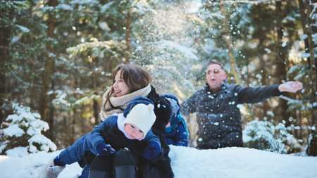 Family playing in snowy forest, laughing while tossing snow, capturing winter bonding moment between parents and childrenの写真素材