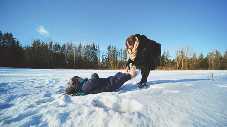 Caring mother adjusting winter boots, bonding with smiling child near snow covered trees during...