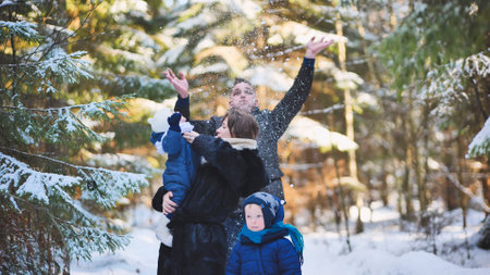 Cheerful family tossing snowflakes, enjoying winter moments amid snow covered woodland landscapeの写真素材
