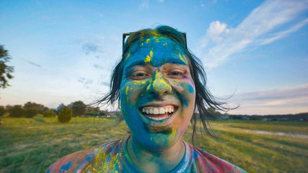 Young person laughing with colorful powder paint covering face and clothes at a college event