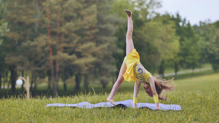 Flexible young gymnast executing dynamic cartwheel on outdoor green mat during sunny summer dayの写真素材
