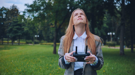 Female professional flying drone in sunny park, smiling with enthusiasm while navigating remote controlled technology outdoorsの写真素材