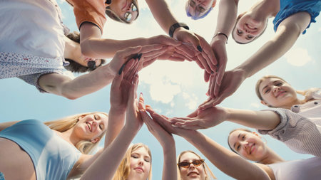 Friends at school joining hands in a circle, representing unity, teamwork, and friendship under a...
