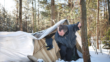 Homeless alcohol addicted man leaving his makeshift tent in a snowy forest, struggling with...