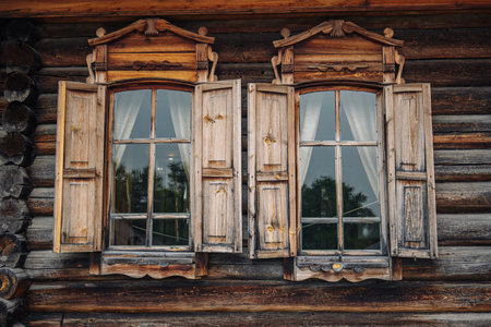 Open vintage wooden windows with carved architraves and slightly open shutters on a traditional russian log cabinの写真素材