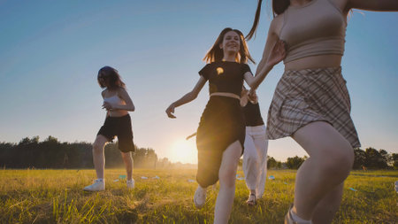 Four high school students enjoying a sunset run across a sunlit field, celebrating the freedom and thrill of summer breakの写真素材