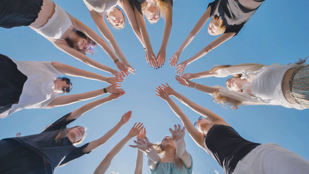 High school students come together in unity, teamwork, and collaboration, forming a circle against a blue skyの写真素材