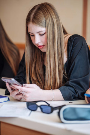 High school student using mobile phone in classroom while studying, with virtual reality headset and sunglasses on deskの写真素材