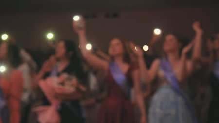 Group of students waving illuminated cell phones at graduation party, celebrating friendship and...