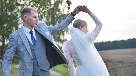Newlyweds dancing, embracing golden sunset light in open field, sharing intimate wedding moment with...