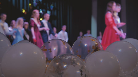 Jubilant graduates standing on stage, embracing amid vibrant balloons, marking academic milestone...