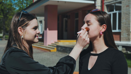 Two high school girls using a makeup brush during a school break, having fun togetherの写真素材