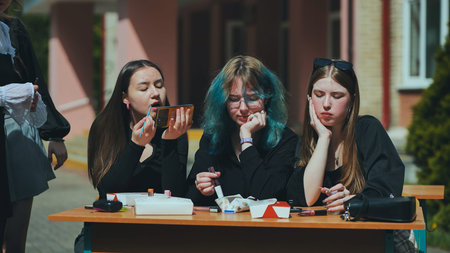High school girls having a carefree makeup session outdoors during their break, enjoying the...