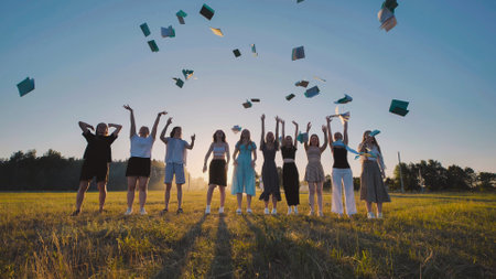 Group of cheerful high school students throwing books up in the air celebrating summer vacation in a field at sunsetの写真素材