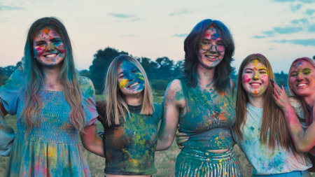 School friends covered in colored powder paint embrace each other joyfully during a playful outdoor gatheringの写真素材