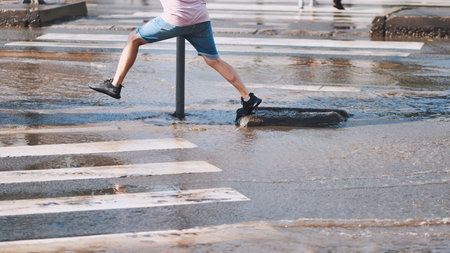 Tourist jumping across waterlogged intersection, preventing wet shoes during urban rainstorm