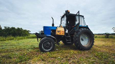 Blue tractor staying parked in a mowed field under cloudy sky