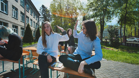 High school students celebrating friendship and academic success with high fives outdoors on a sunny school dayの写真素材