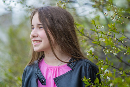 Happy teen girl enjoying spring season posing near blooming tree, wearing black leather jacket and pink shirtの写真素材