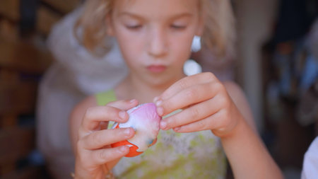 A little girl unfolds and eats a chocolate egg with toys.の写真素材