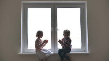 Silhouette of children playing hand on window sill.の写真素材