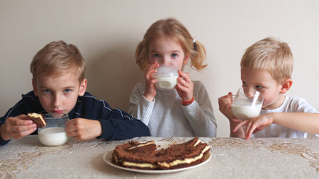 Children at the table eat milk and cookies.の写真素材