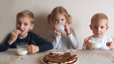 Children at the table eat milk and cookies.