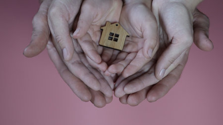 The hands of the mother and father with the child hold the figure in the form of a house on a pink background.の写真素材