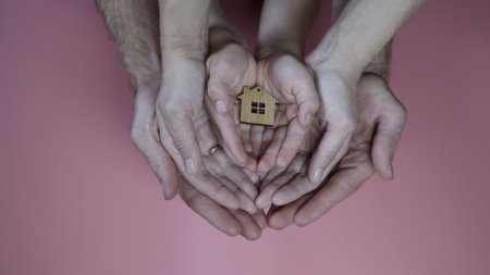 The concept of saving a friendly family. The hands of the mother and father with the child hold the figure in the form of a house.の写真素材
