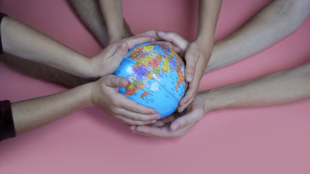 A friendly family hold the earth globe in their hands on a pink background. The concept of saving the world.の写真素材