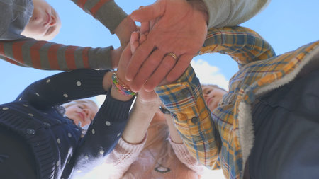 The concept of cohesion. Friendly family joins hands against the blue sky.