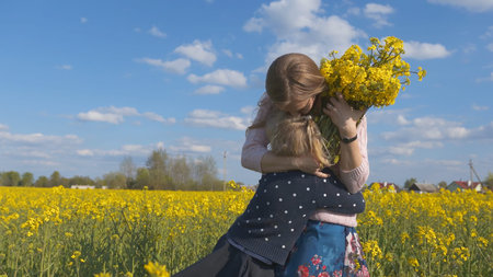 Grateful daughter gives her mother flowers in a rapeseed field.の写真素材
