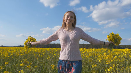 Happy girl with a bouquet of rapeseed flowers in a yellow rapeseed field.