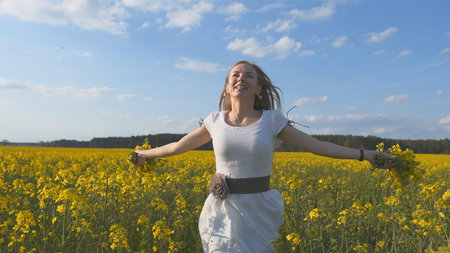 Happy girl in a white dress with a bouquet of rapeseed flowers in a yellow rapeseed field.