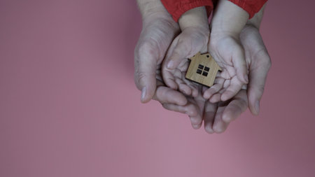 The hands of the mother and father with the child hold the figure in the form of a house on a pink background.の写真素材